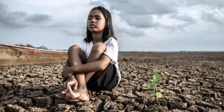 Una niña está sentada en un paisaje desértico como reflejo de los efectos de la crisis climática.
