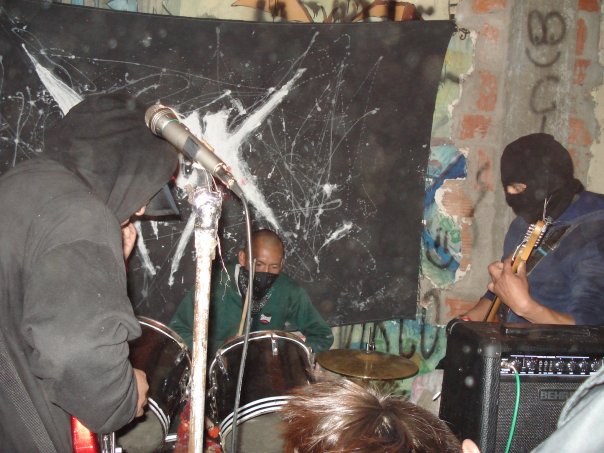 Fotografía de tres músicos del movimiento anarco punk en El Alto durante un concierto en un escenario itinerante.