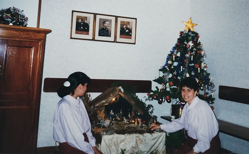 Dos niñas asistentes a la escuela de mucamas posan para la foto en un arbol y nacimiento de navidad