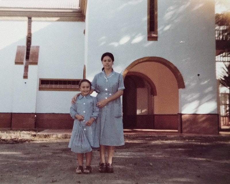 Una asistente de la escuela de mucamas del Opus Dei posa en la puerta junto a una niña, ambas con uniforme