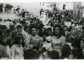 Ofelia y Liz Karina posando a los costados de una madre con su bebé en la calle Junín de la ciudad de Oruro, durante una celebración del Carnaval de Oruro en los años 70, en una fotografía en blanco y negro.