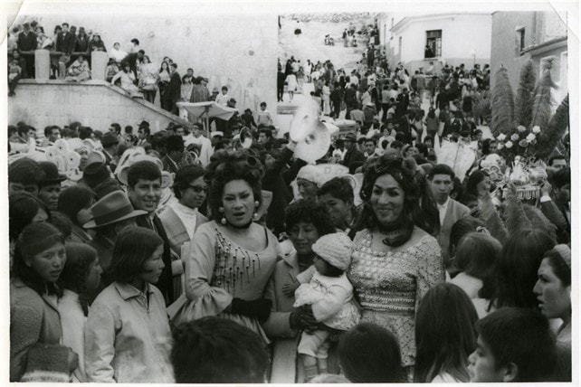 Ofelia y Liz Karina posando a los costados de una madre con su bebé en la calle Junín de la ciudad de Oruro, durante una celebración del Carnaval de Oruro en los años 70, en una fotografía en blanco y negro. 