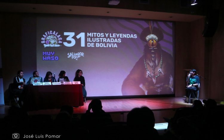 Evento de presentación del libro 31 mitos y leyendas ilustradas de Bolivia. En el fondo del escenario la portada del libro, delante artistas que participaron del libro y la presentadora del evento.