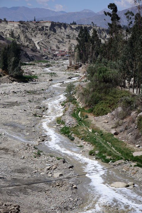 El río La Paz en su bajada hacia Mecapaca, La Paz. A la izquierda un terreno pedregoso, a la izquierda una arboleda y por el medio el cauce de agua. 