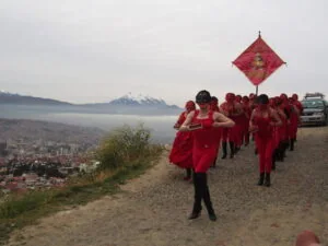 Un fotograma de la película Revolución Puta en la que un grupo de mujeres vestidas de rojo camina por una ladera de la ciudad de La Paz, con el Illimani de fondo.