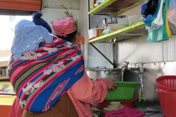 Una vendedora de comida carga  a su niño mientras alista los alimentos para ofrecer almuerzos en el Mercado Lanza.