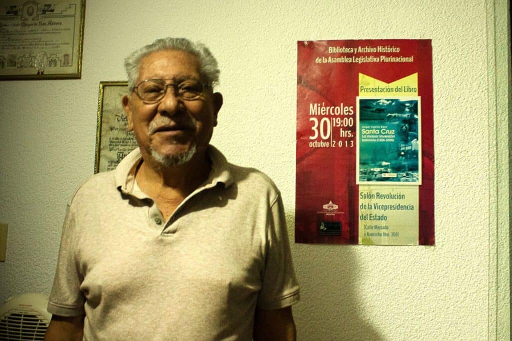 Ángel Castro junto al afiche de 2013 del lanzamiento de su libro