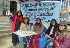 "Muro de la vergüenza" Cinco mujeres del colectivo Mujer de Plata en Potosí posan delante de una lona que dice "Si no paga pensión, NO merece celebración". Estudio Jurídico Callejero, intervención urbana feminista realizada para el día del padre en 2024