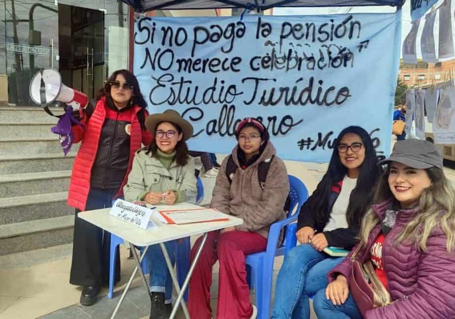 "Muro de la vergüenza" Cinco mujeres del colectivo Mujer de Plata en Potosí posan delante de una lona que dice "Si no paga pensión, NO merece celebración". Estudio Jurídico Callejero, intervención urbana feminista realizada para el día del padre en 2024