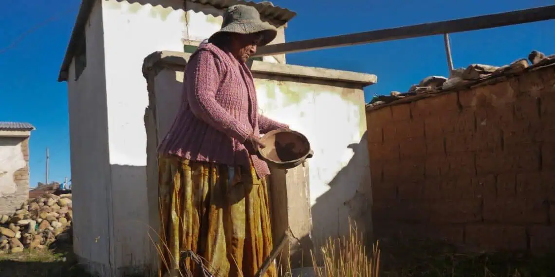 Una anciana aymara iluminada por los rayos de sol de la mañana, sostiene un cuenco sin agua en el altiplano boliviano.