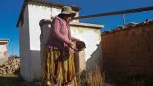 Una anciana aymara iluminada por los rayos de sol de la mañana, sostiene un cuenco sin agua en el altiplano boliviano.