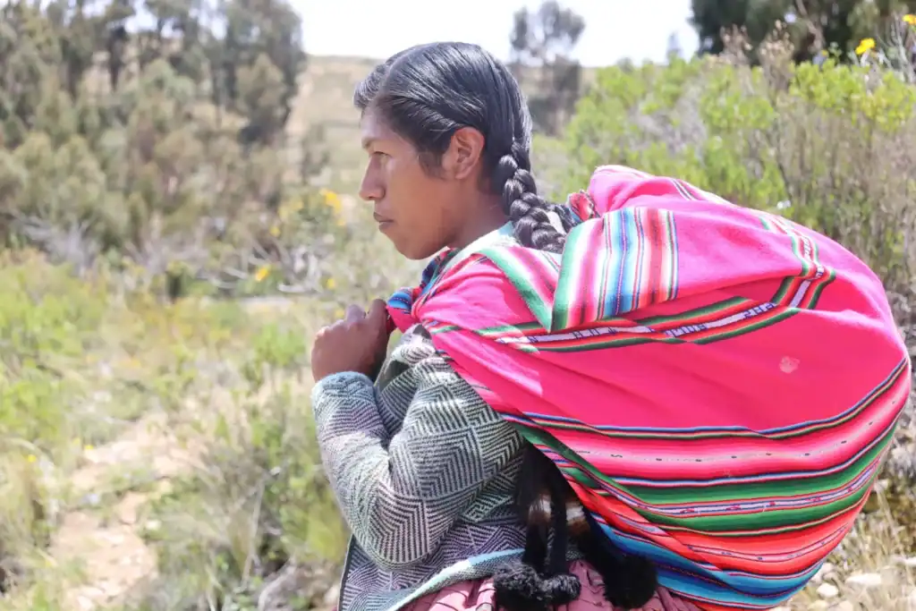 Fotografía de Joanna Lizzeth Gonza, mujer indígena transgénero, vestida con pollera, cargando un aguayo en su comunidad